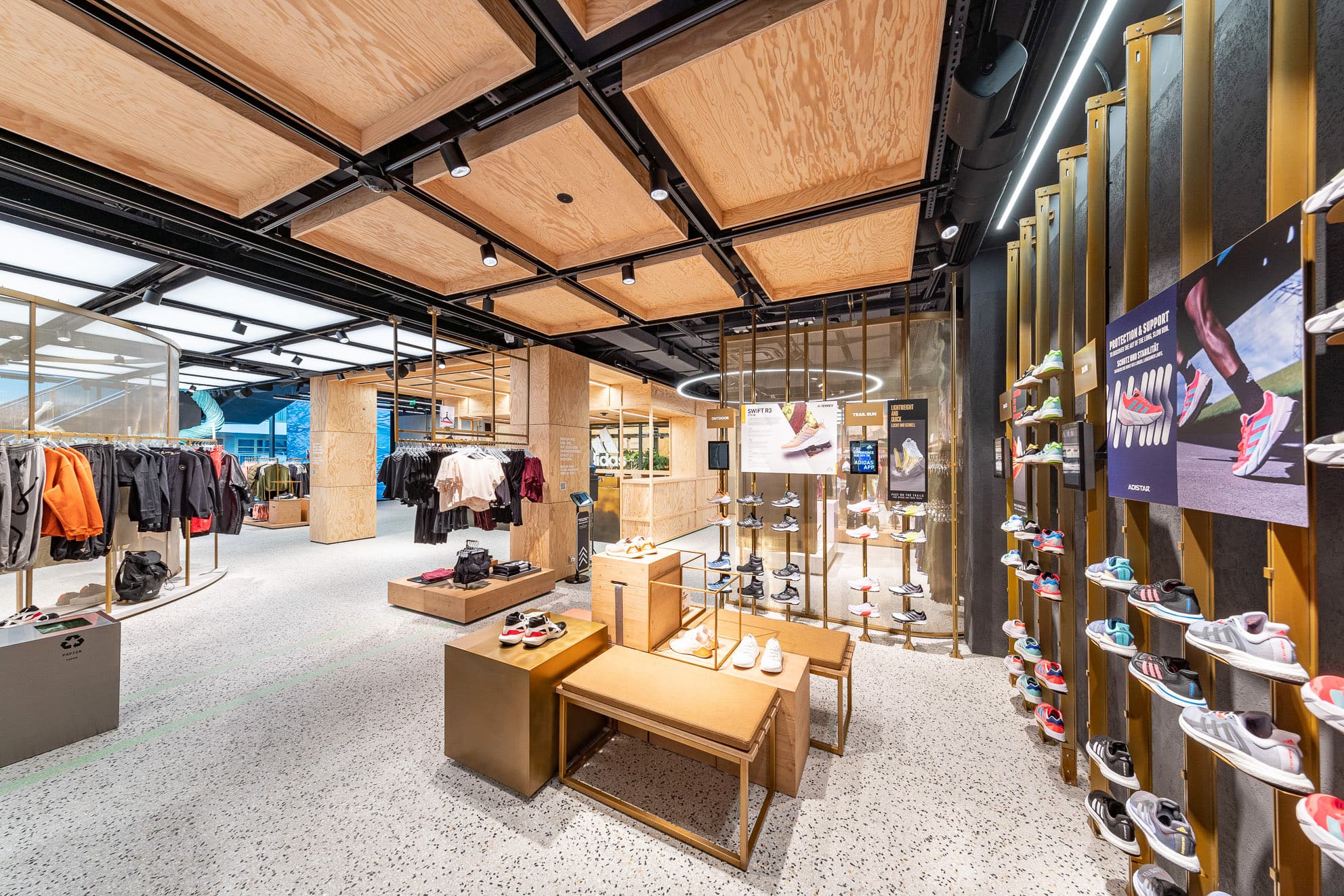 Sportgeschäft mit Schuhwand, Bekleidungsständern, Holzregalen und abgehängten Holzdeckenpanelen.