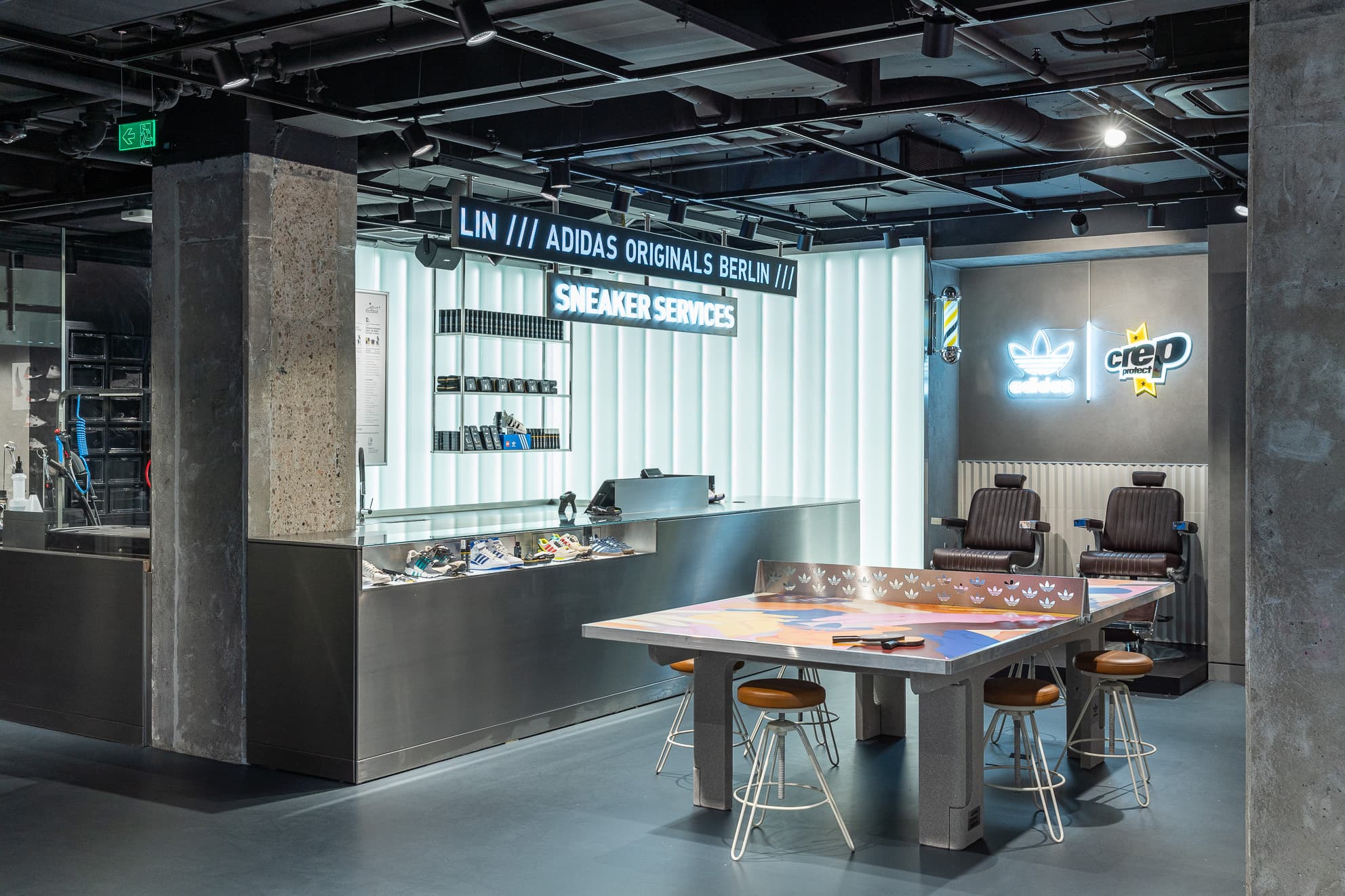Sneaker-Servicebereich im Adidas Originals Store Berlin mit Theke, Arbeitstisch und zwei Stühlen.