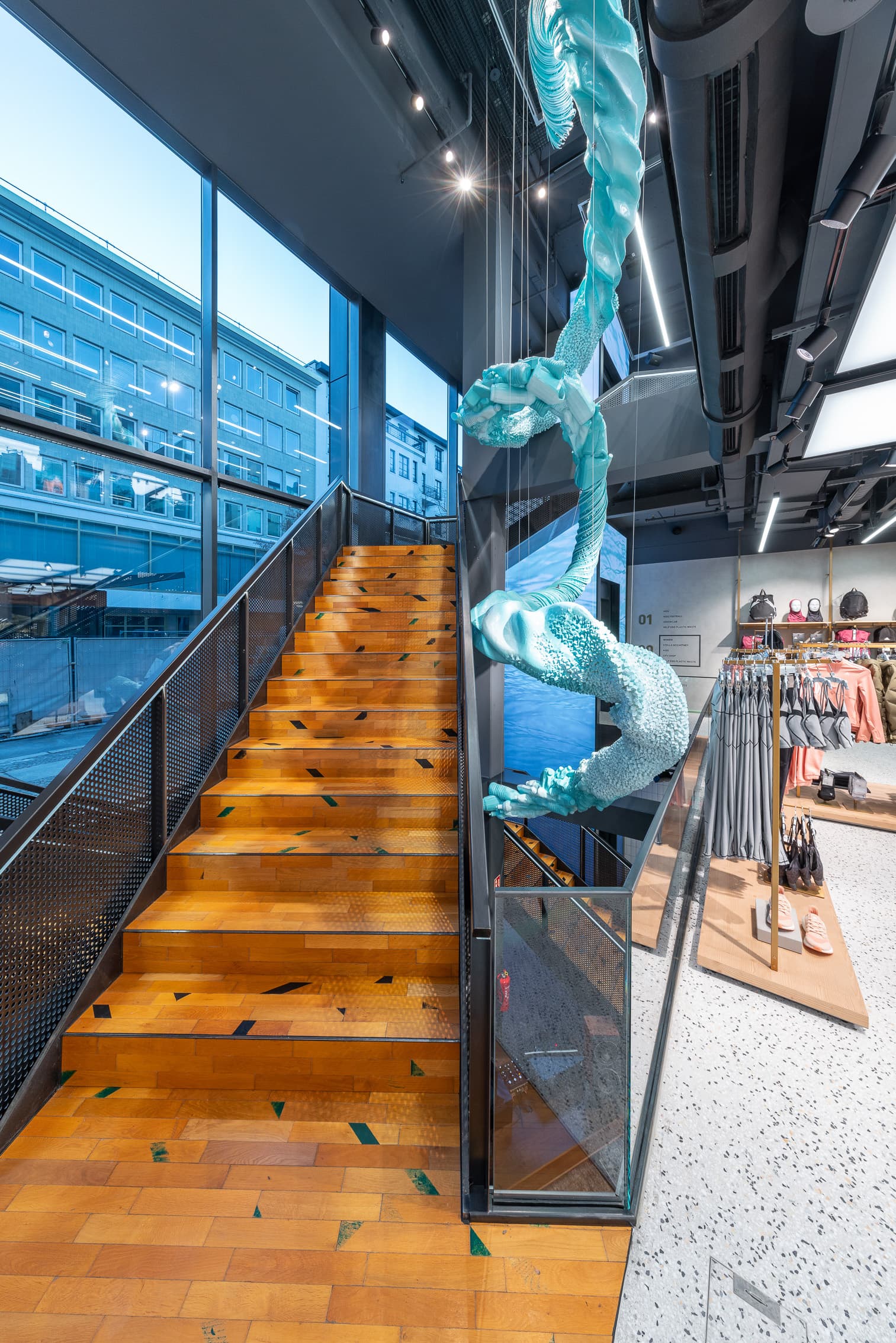 Holztreppe in einem Sportgeschäft mit großer türkisfarbener Hängeskulptur und Sportbekleidung.