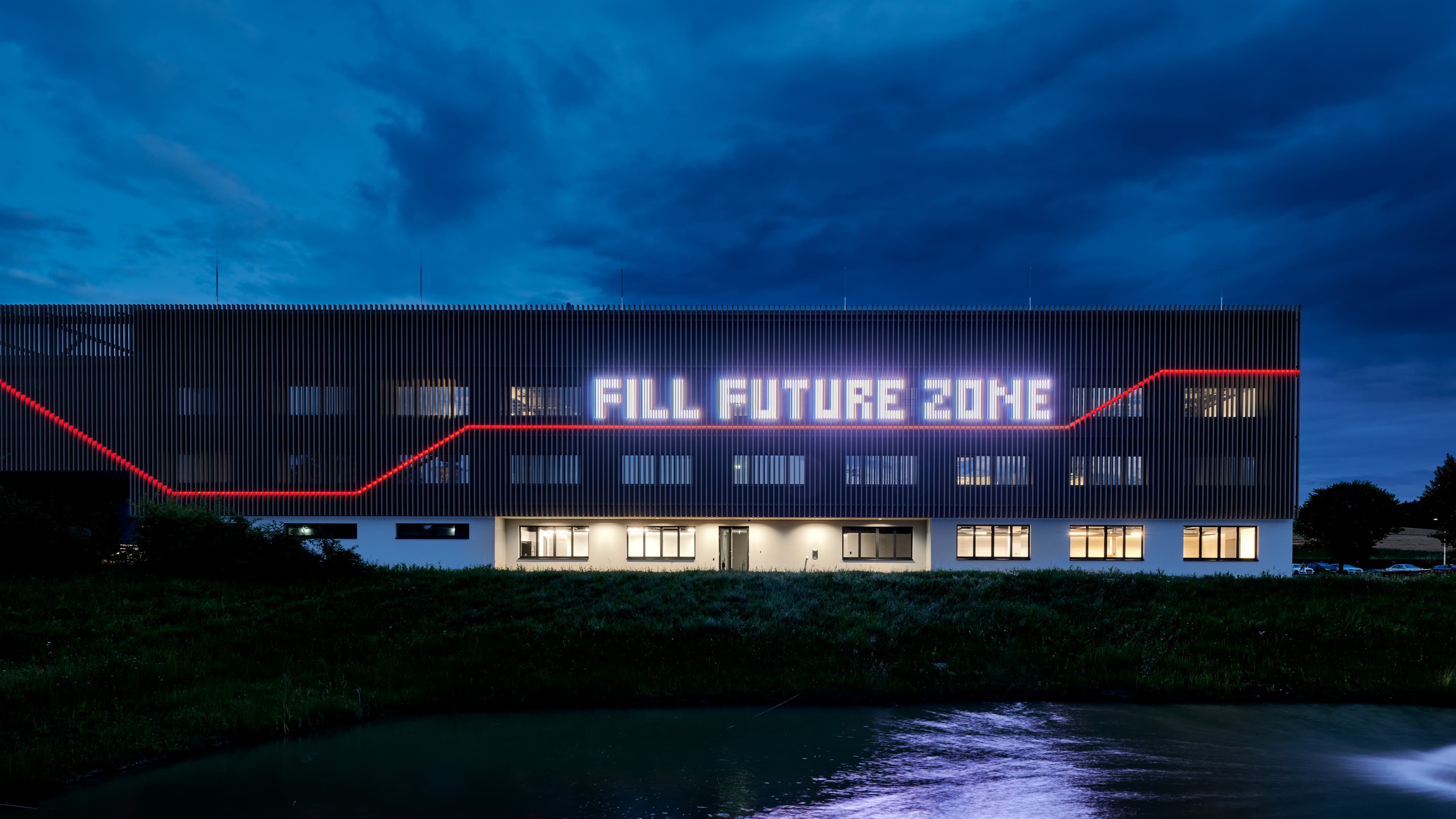 Außenansicht eines Gebäudes bei Nacht mit beleuchteter Schrift „Fill Future Zone“.