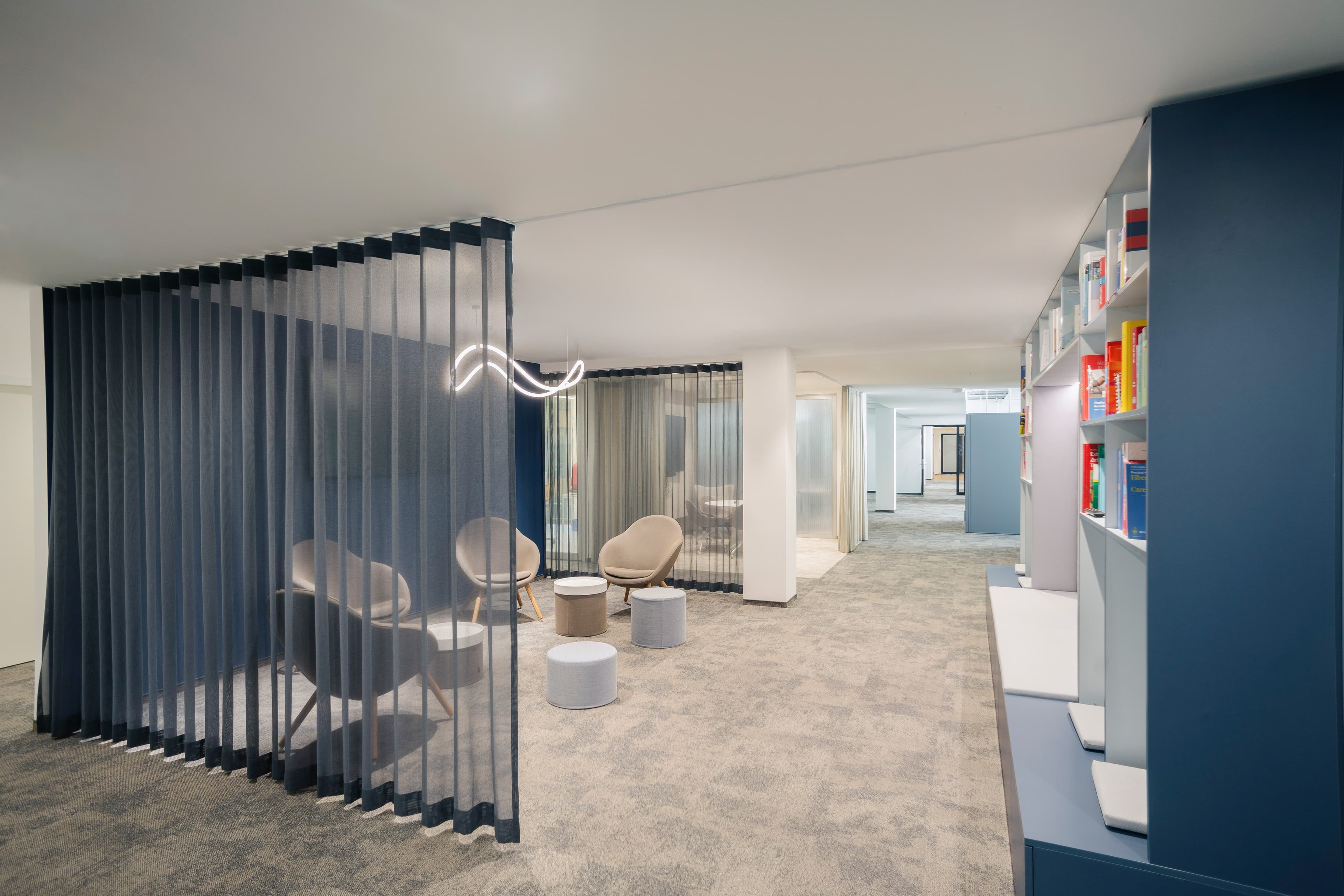 Bürobereich mit Vorhangabtrennung, Sitzgruppe, Bücherregal und langen Flur.