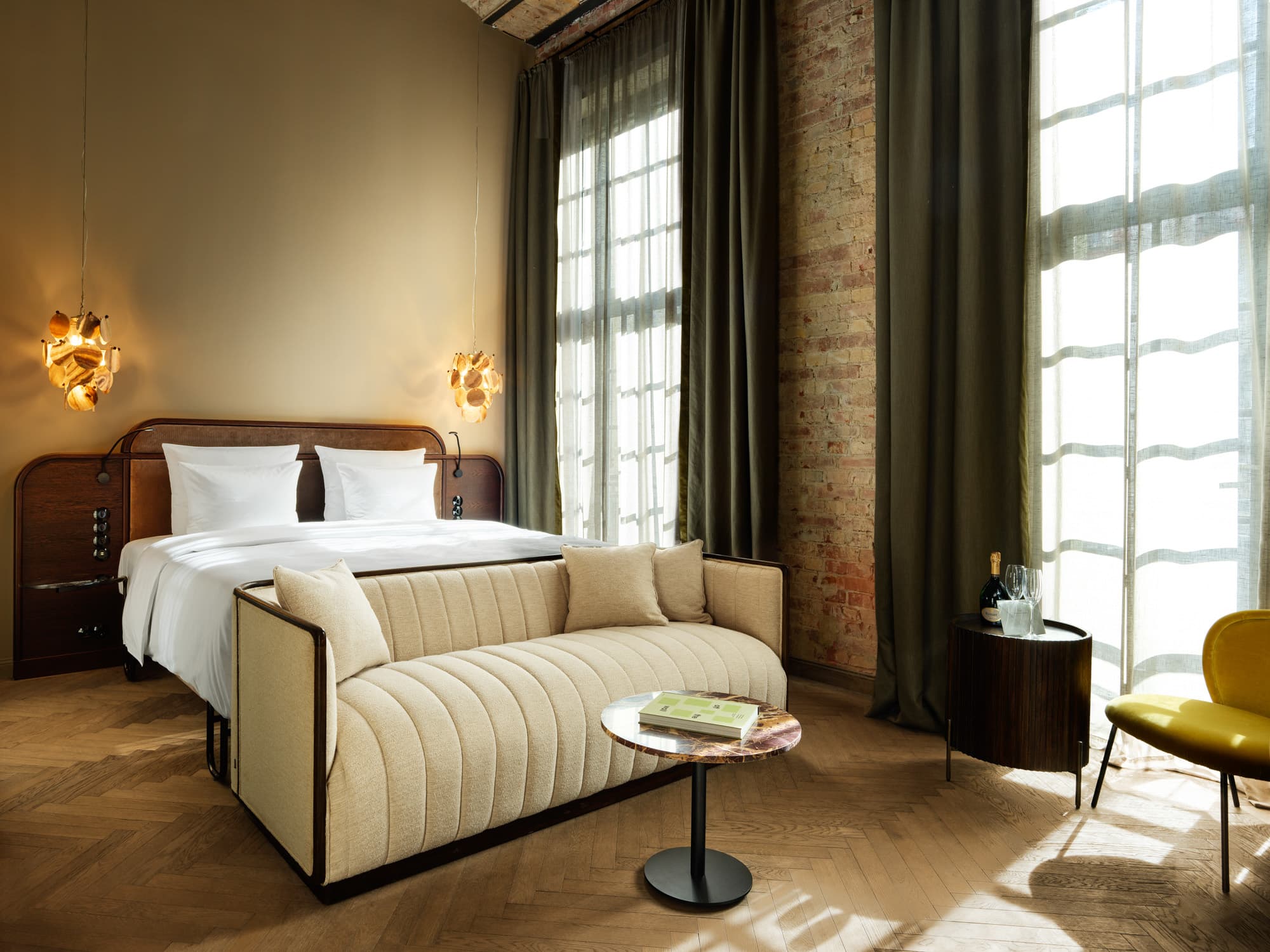Hotelzimmer mit Doppelbett, gepolstertem Sessel und hohen Fenstern in historischem Mauerwerk.