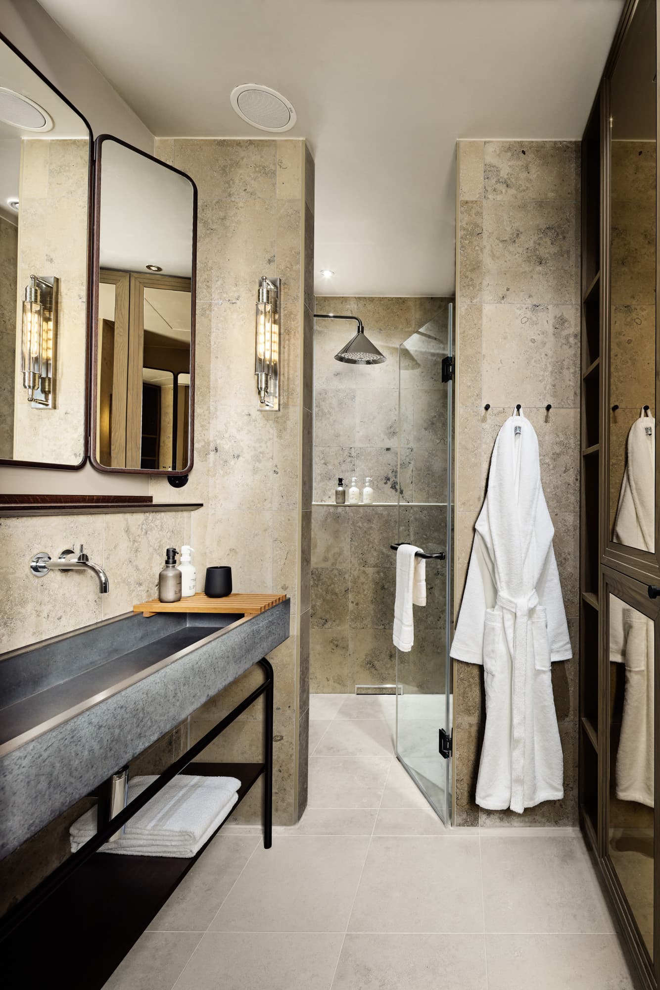 Badezimmer mit dunklem Waschtisch, großem Spiegel, Dusche und weißem Bademantel.