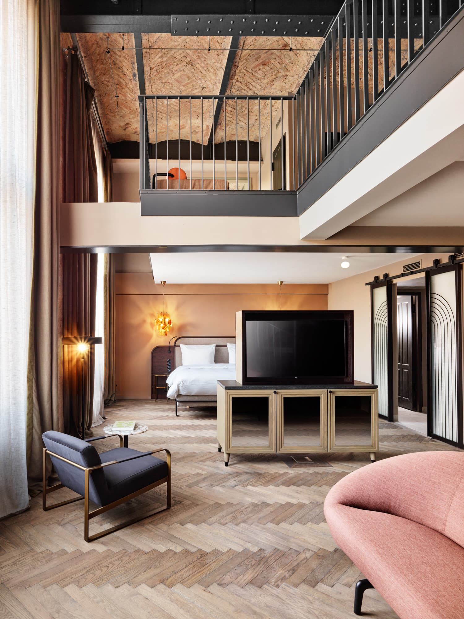 Maisonette-Zimmer mit Fernseher, Sitzmöbeln, Galerie und großer Fensterfront.