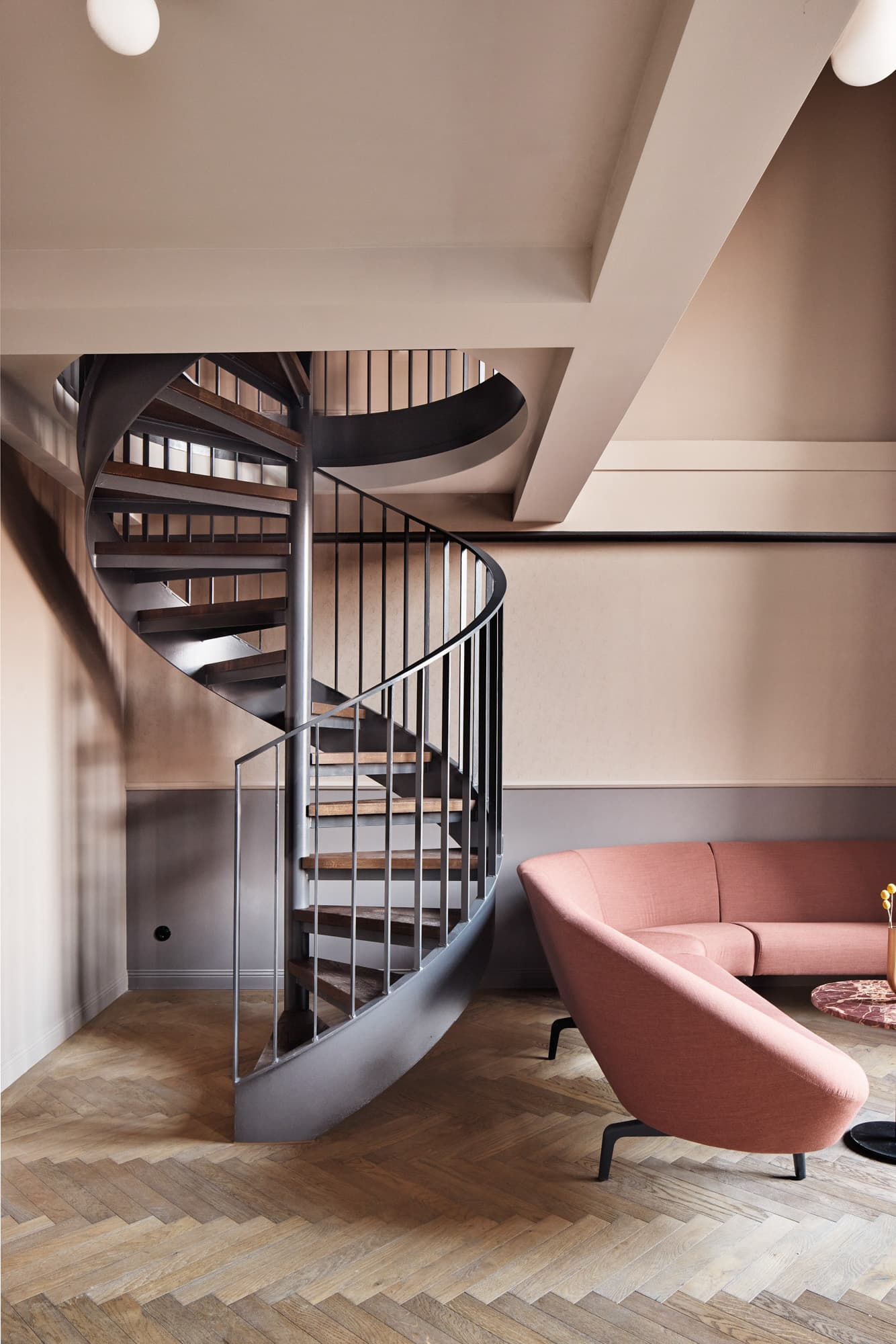 Wendeltreppe in einem Hotelzimmer mit rosa Sessel und gemustertem Holzboden.