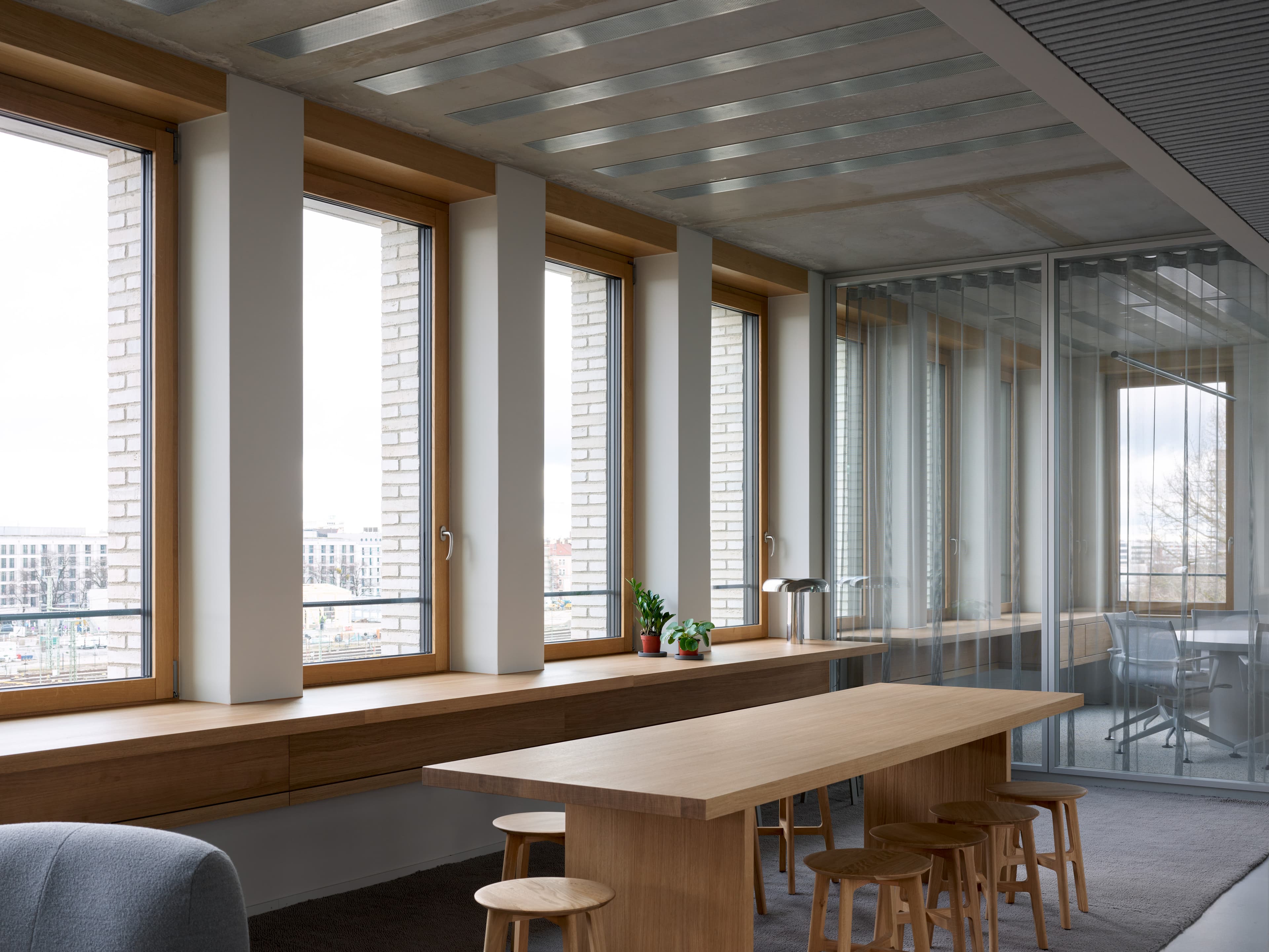 Heller Bürobereich mit Holztisch, Sitzbank am Fenster und Blick auf die Stadt.