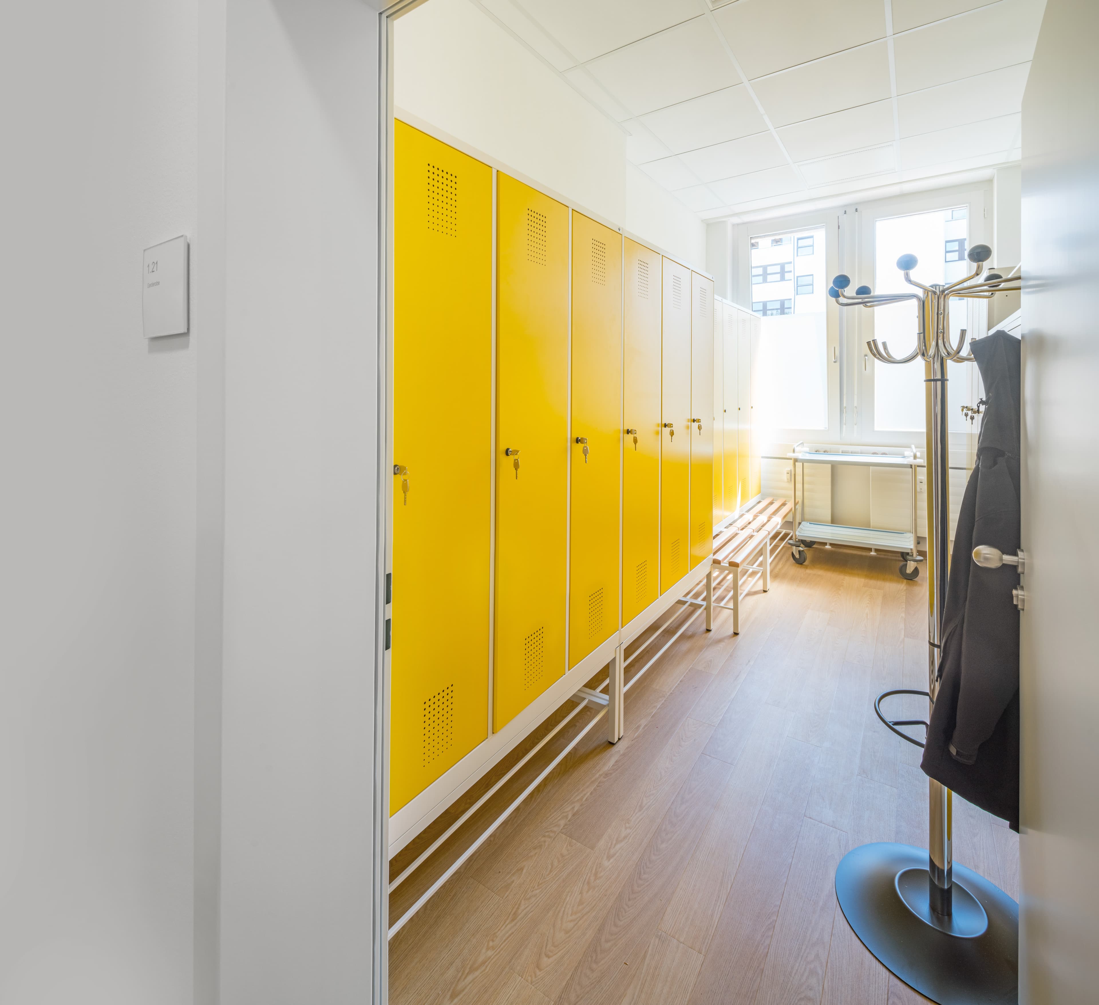 Gelbe Spinde mit Sitzbank und Garderobenständer in einem hellen Umkleideraum mit Holzboden.