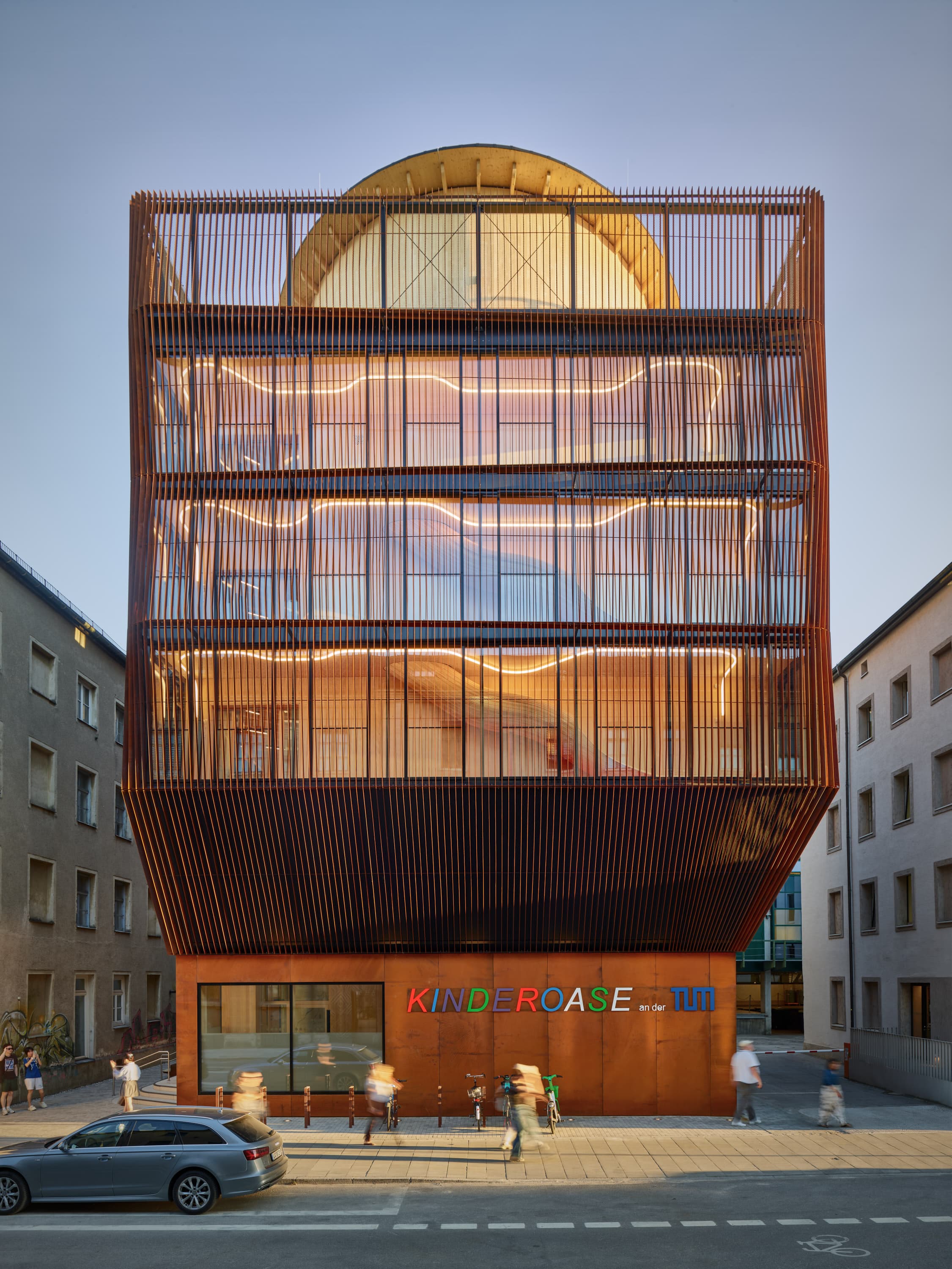 Mehrgeschossiges Gebäude mit rostfarbener Lamellenfassade und Schriftzug „Kinderoase an der TUM“