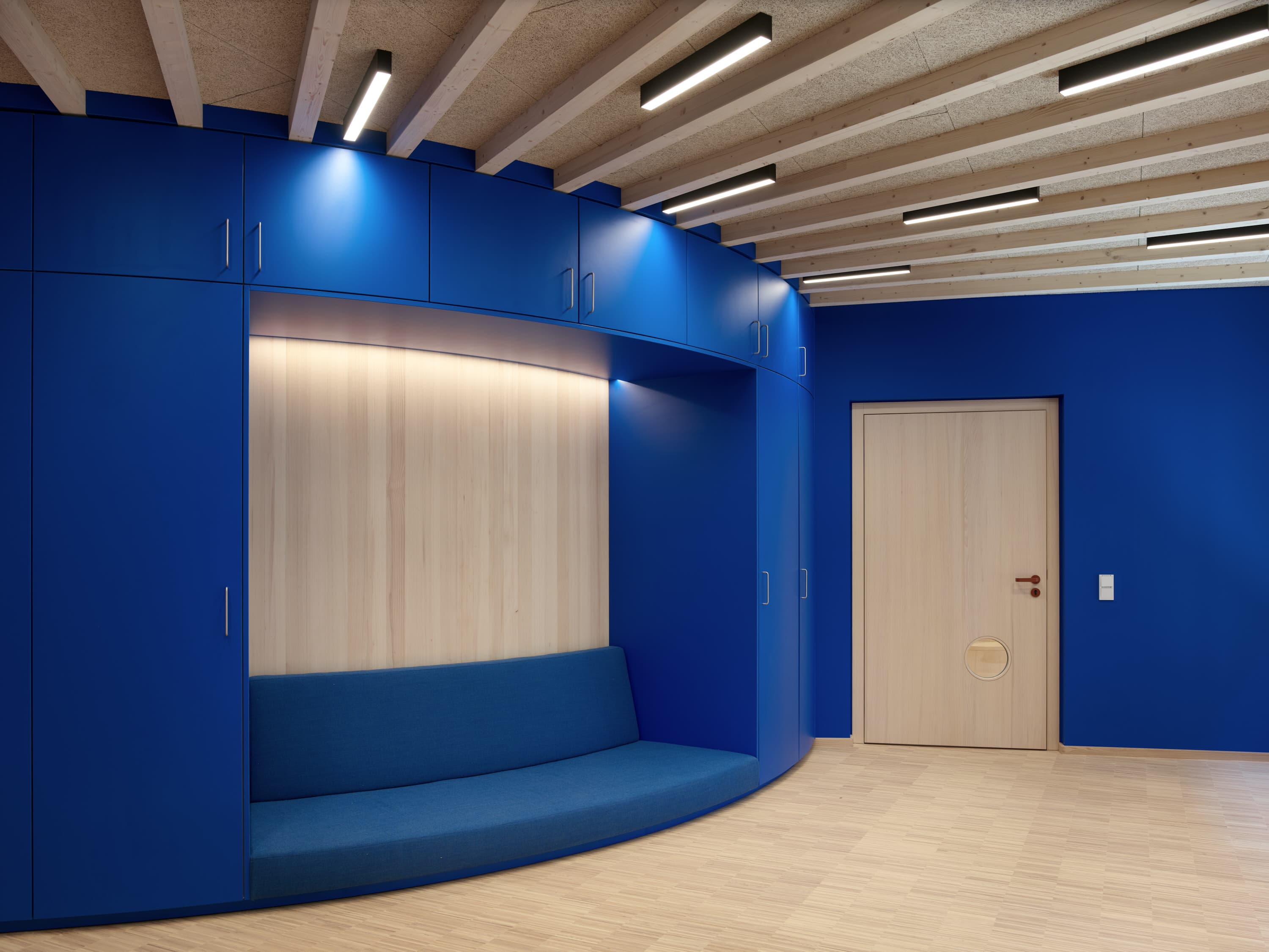 Blauer Einbauschrank mit gepolsterter Sitznische in einem Raum mit Holzbalkendecke.