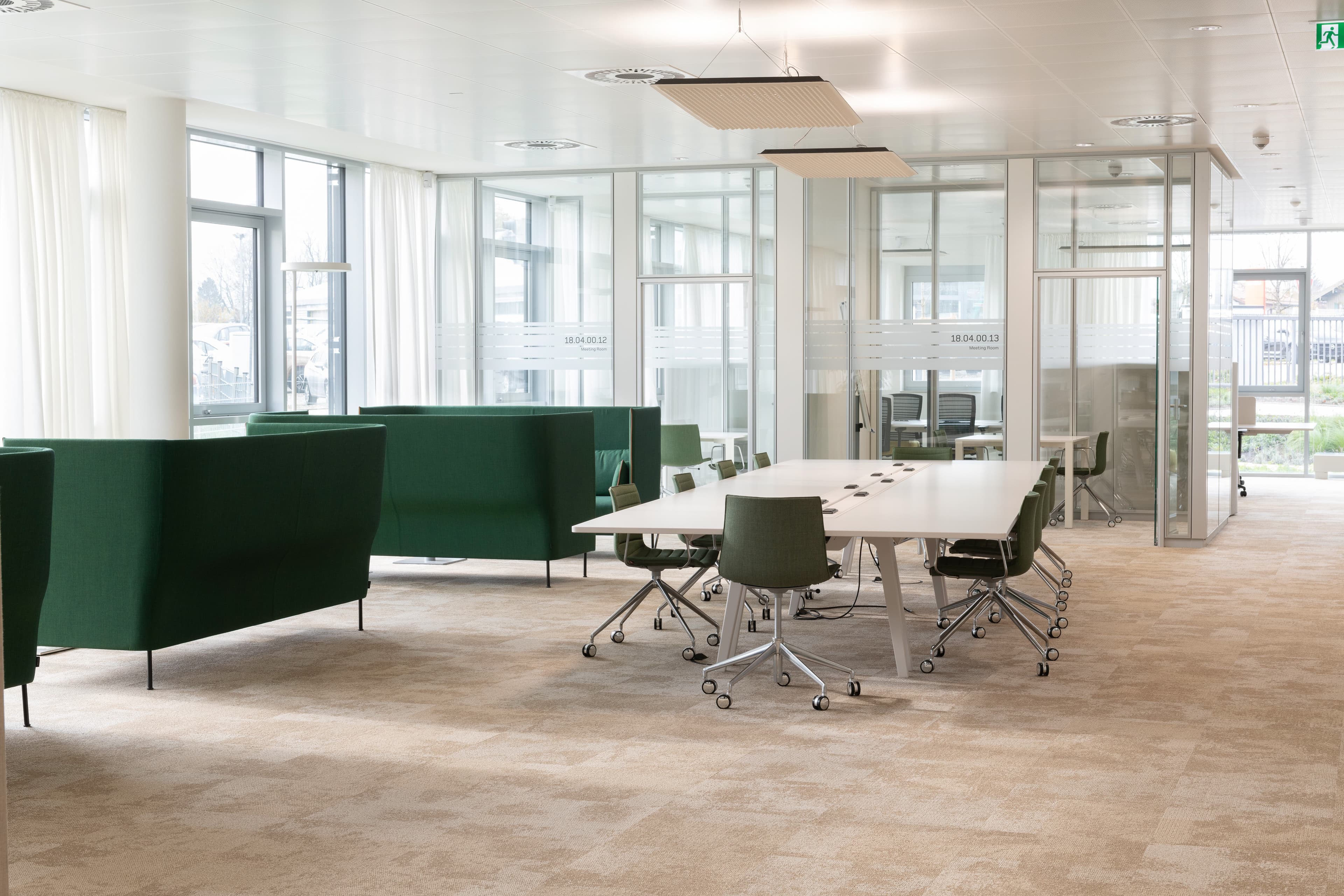 Moderner Besprechungs- und Lounge-Bereich mit grünen Sitzmöbeln, Tischgruppen und gläsernen Trennwänden.