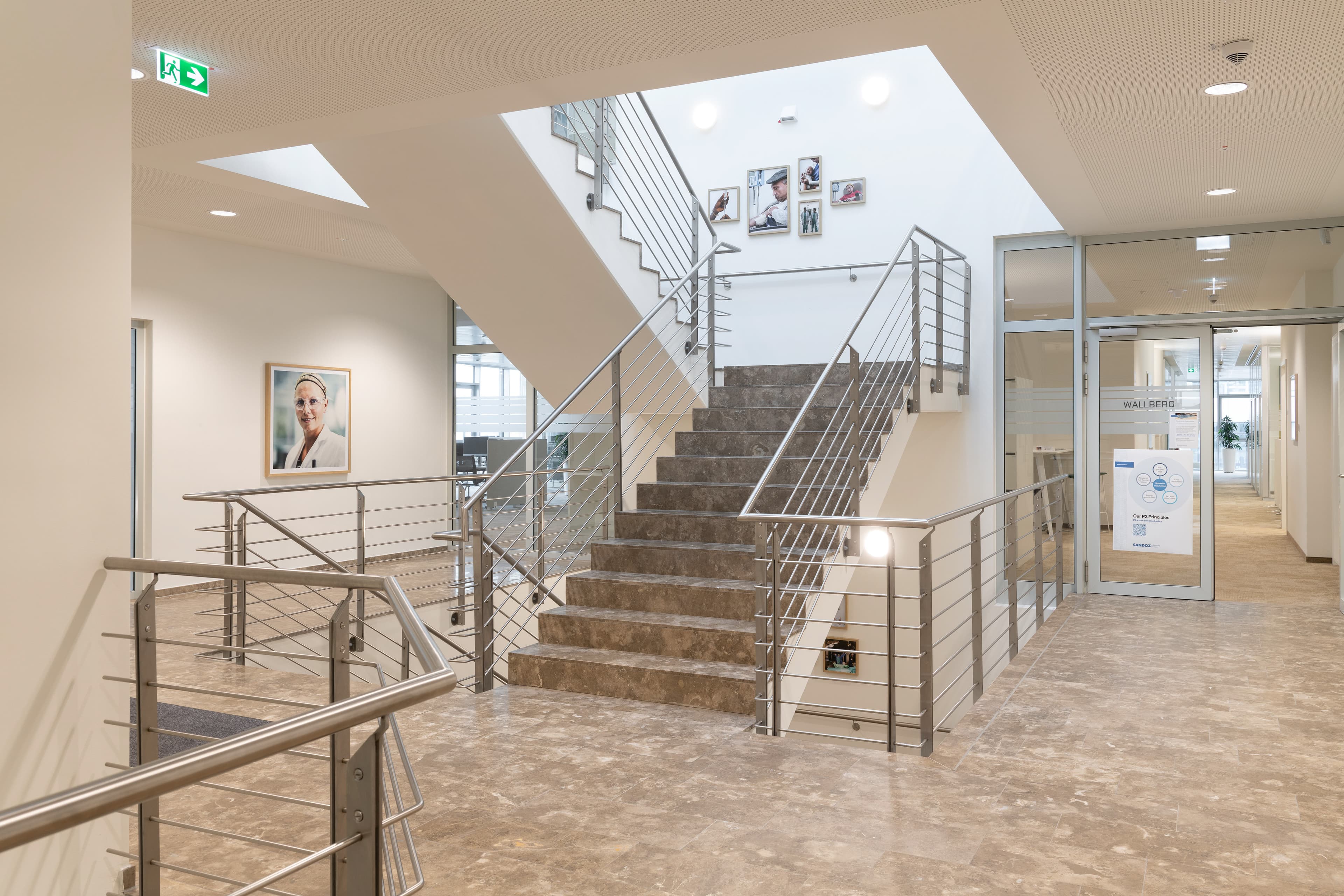 Offenes Treppenhaus mit breiter Treppe, Metallgeländern und viel Tageslicht.