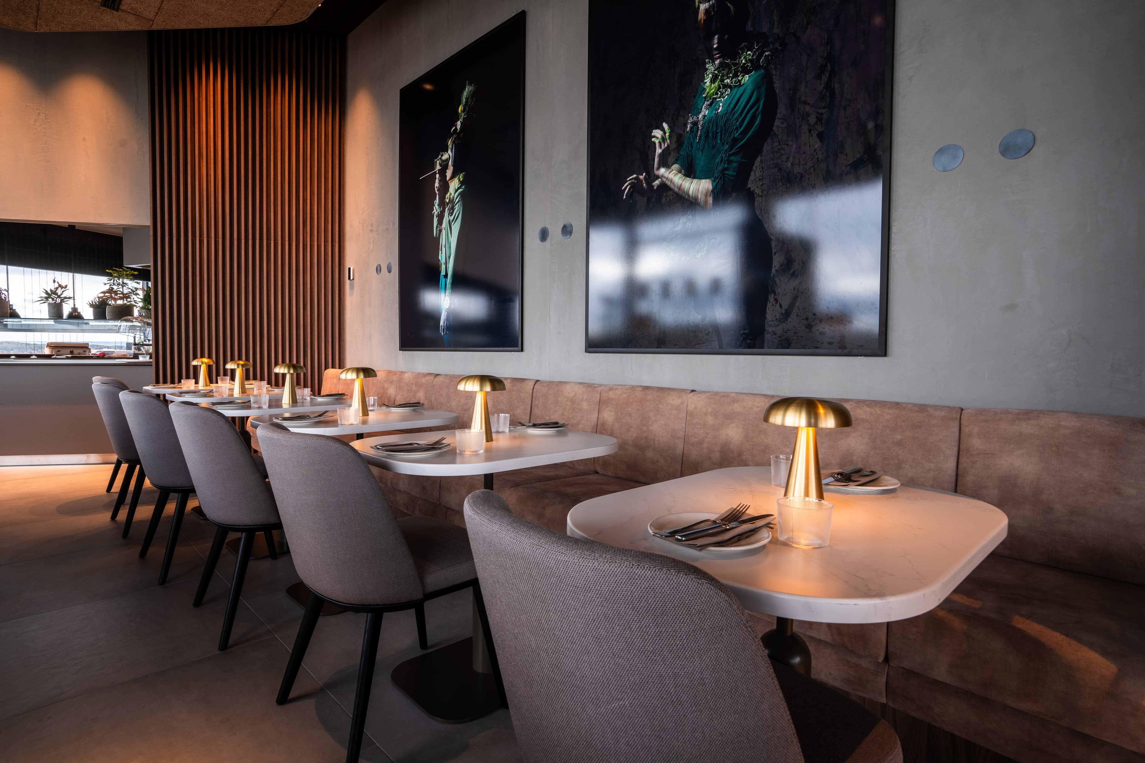 Modernes Restaurant mit gedeckten Tischen, grauen Stühlen, Sitzbank, Tischleuchten und großformatiger Wandkunst.