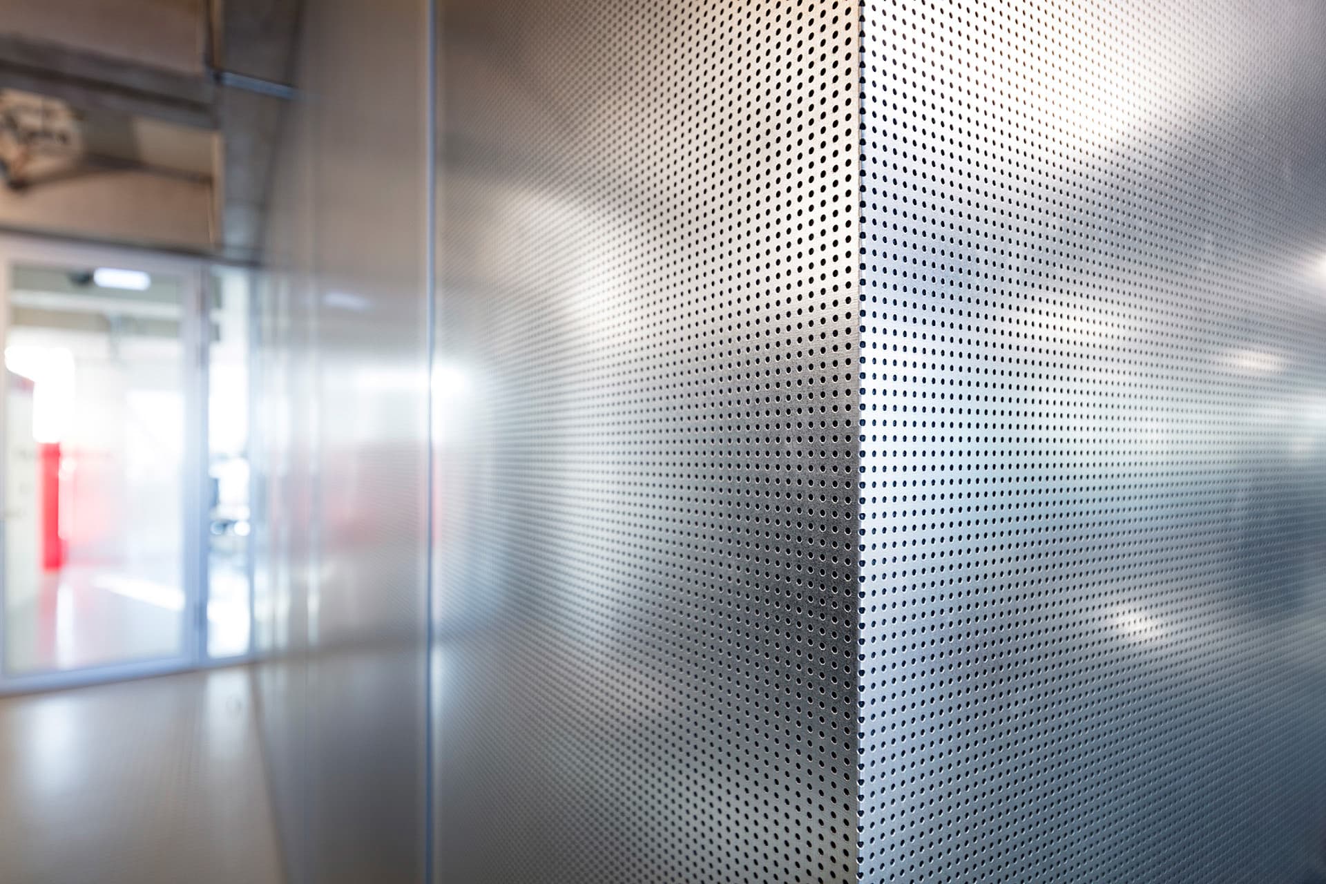 Detailansicht einer transparenten beziehungsweise perforierten Innenwand mit unscharfem Blick in den angrenzenden Raum.