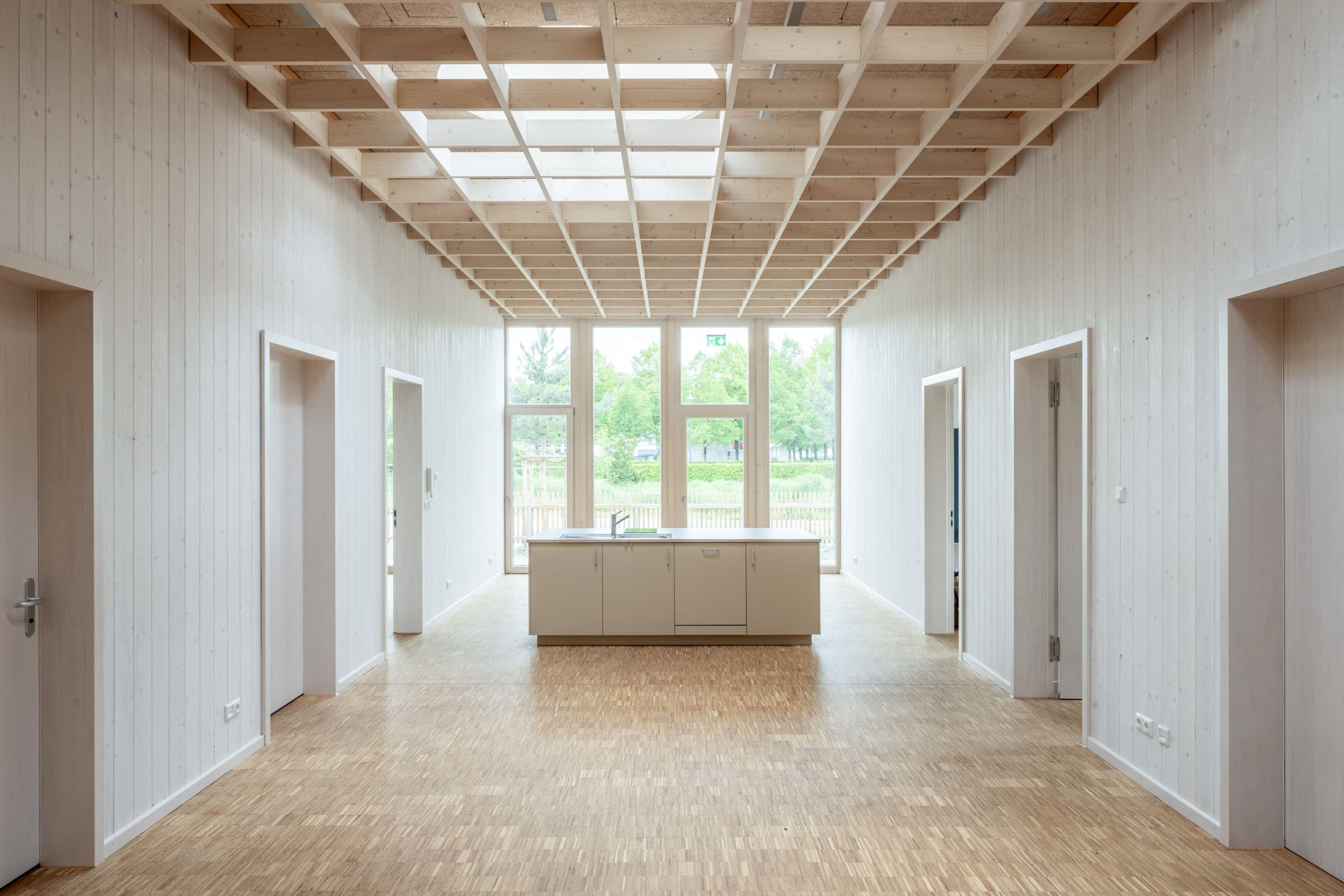 Heller Flur mit Holzrasterdecke, weißen Türen und Fenster am Raumende.
