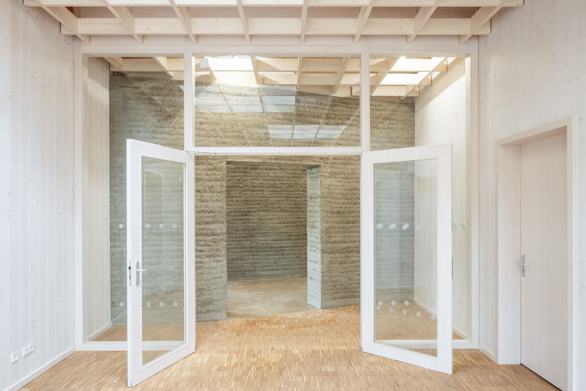 Eingangsbereich mit Holzrasterdecke, Glastüren und strukturierten Wänden.