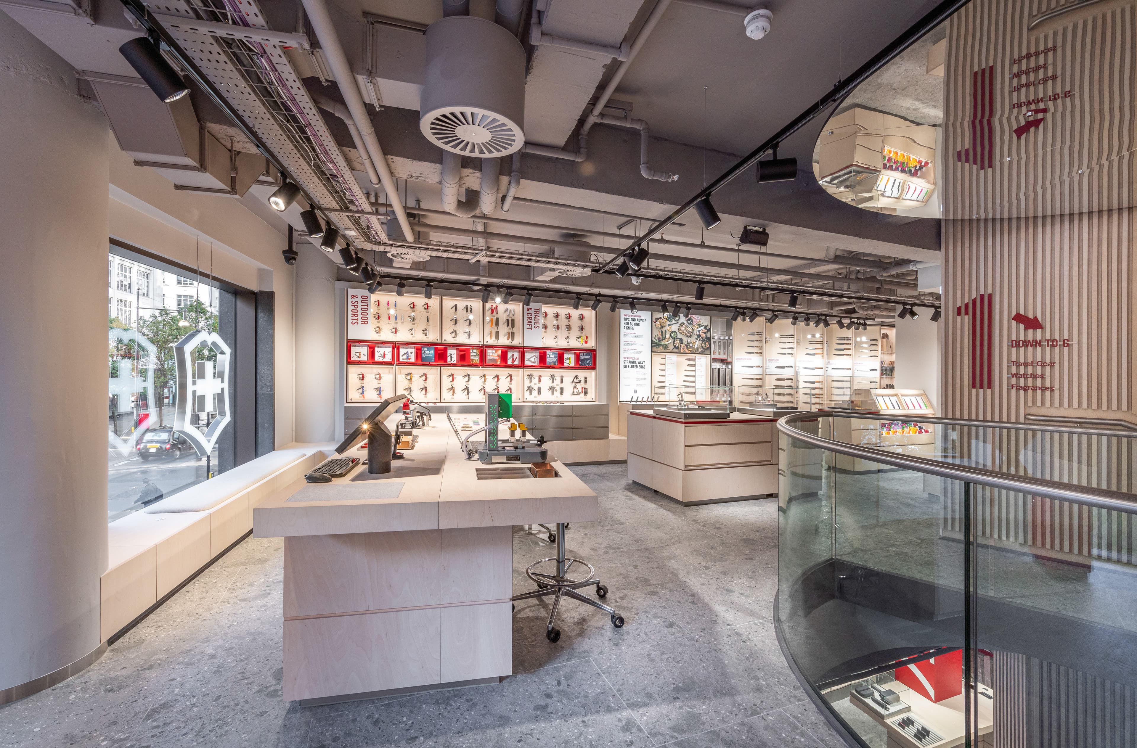 Heller Verkaufsbereich mit zentralem Tisch, roten Produktdisplays und Treppe.