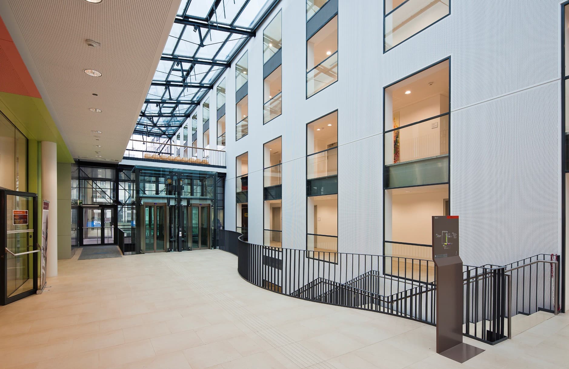 Helles Atrium mit Glasdach, Holzverkleidung, breiten Wegen und offenen Galerien.
