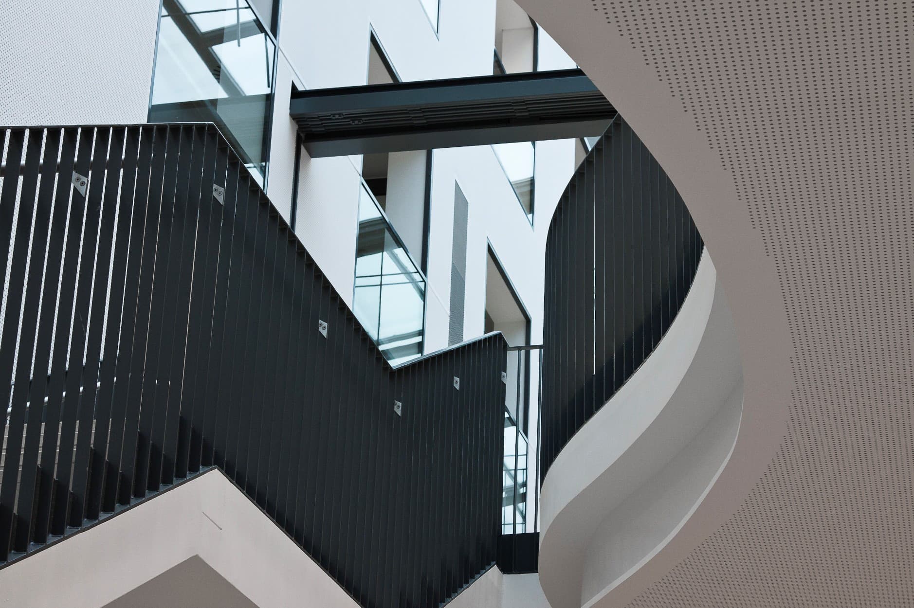 Geschwungene Treppe mit schwarzem Geländer und perforierter Wandverkleidung.