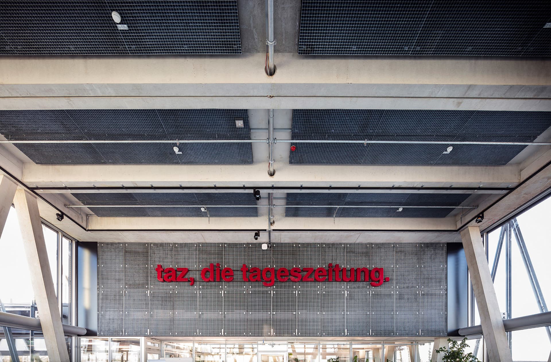 Innenraum mit sichtbarer Deckenkonstruktion und rotem Schriftzug „taz, die tageszeitung“.