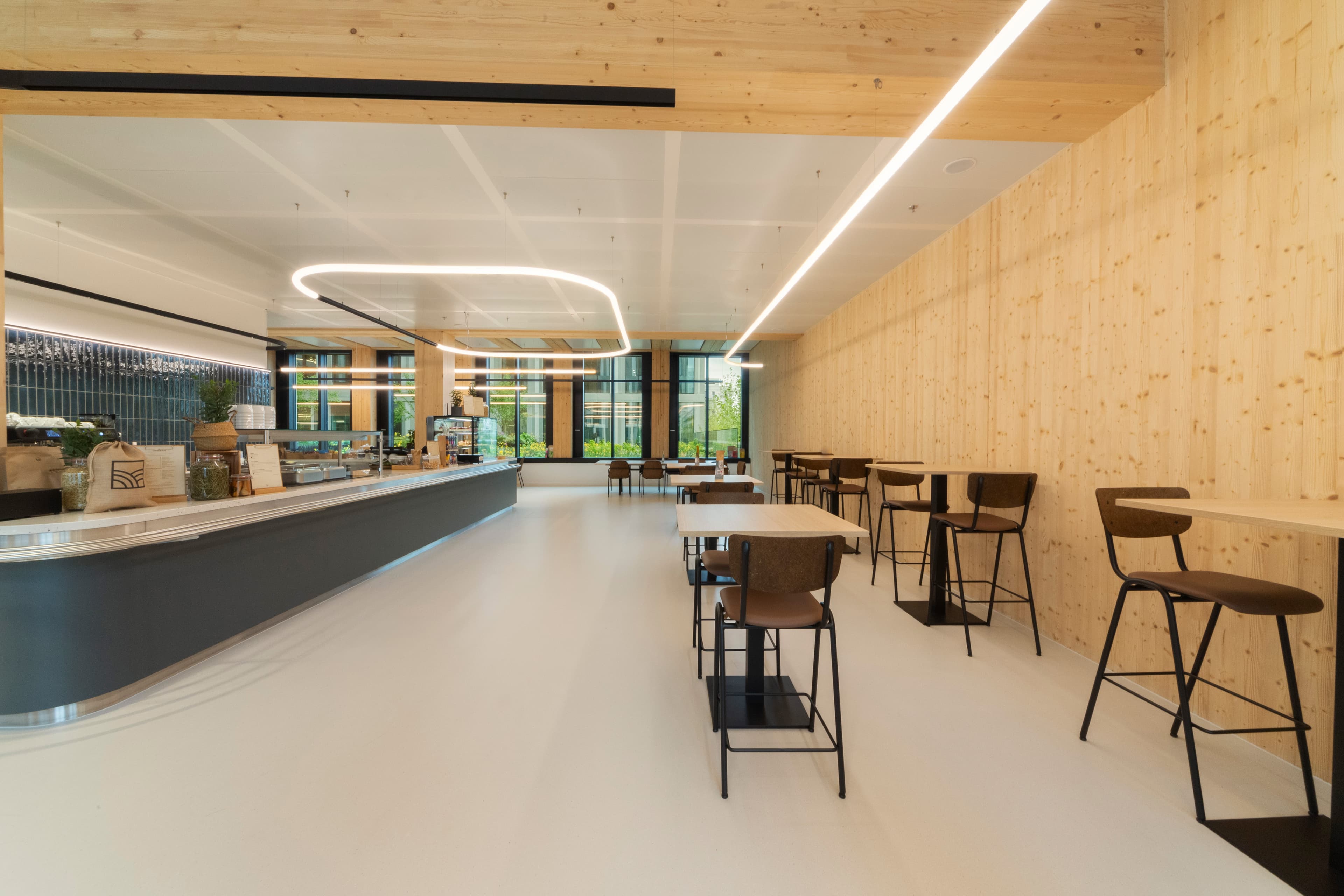 Sitzbereich mit Tischen und Stühlen neben schwarzem Tresen in hellem Holzinterieur.