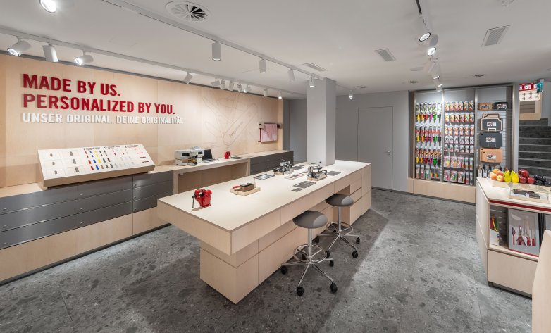 Victorinox Store in Brunnen Ausstellungsfläche im 2. UG, großer Werktisch zur Personalisierung von Taschenmessern vor hölzernem Schild mit Aufschrift "Made by us. Personalized by you. Unser Original. Deine Originalität."