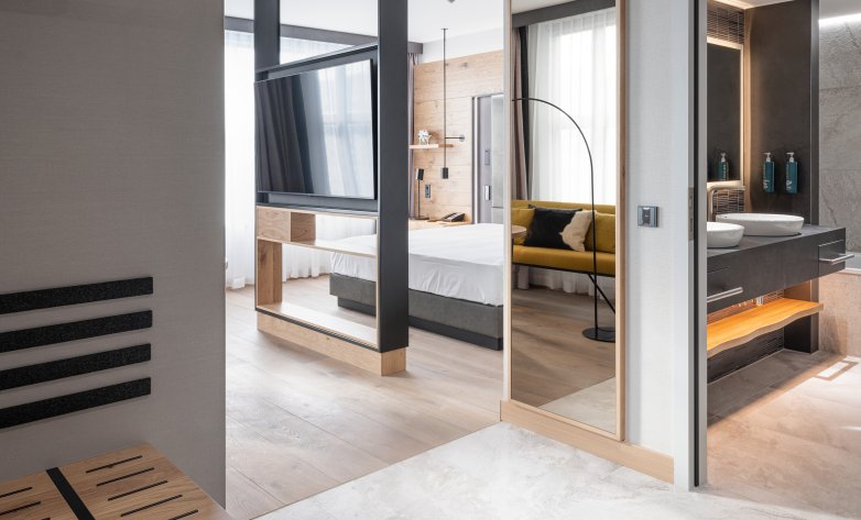 Schlafzimmer mit Eichenboden, Vinyltapete und Holztäfelung, inklusive Blick ins Badezimmer mit Natursteinoptik und Stäbchenmosaik  - Hilton Munich Airport