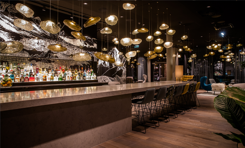 Aufenthaltungsbereich mit Bar, langem Tresen, Desginmöbel und künstlerische Beleuchtung - Motel One Innsbruck 