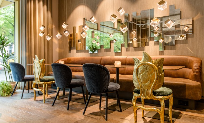 Innenausbau des lichtdurchfluteten Sitzbereiches mit viel Spiegeloptik und toll verzierteten Stühlen in gold im Motel One Würzburg