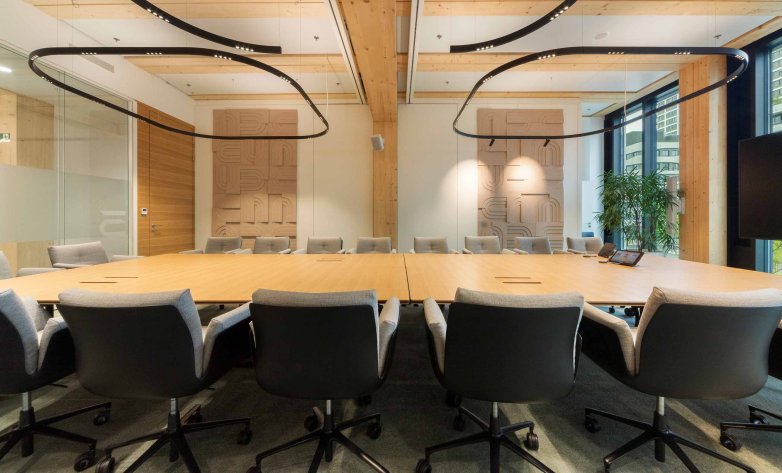 Modern ausgestatteter Konferenzraum mit großem Holztisch, ergonomischen Stühlen und stilvoller Lichtführung: Die offene Architektur und natürliche Materialien schaffen den idealen Rahmen für produktive Meetings in professioneller Atmosphäre.