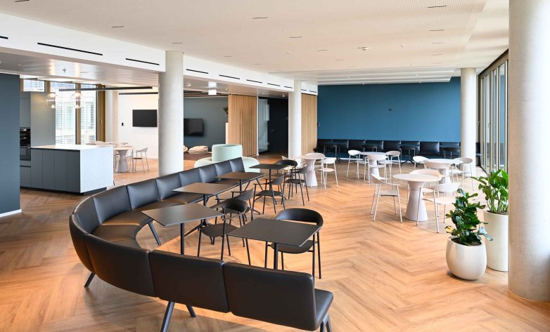 Großzügiger Aufenthaltsbereich mit modernem Lounge- und Cafékonzept. Flexible Sitzgruppen, warme Holzböden und eine offene Raumgestaltung schaffen eine angenehme Atmosphäre für Pausen, Meetings und informellen Austausch. Der integrierte Küchenbereich sowie die lichtdurchflutete Architektur fördern Kommunikation und Wohlbefinden im Arbeitsalltag.