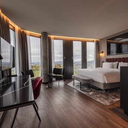 Radisson Blu Stuttgart, Hotelzimmer mit Bett, Schreibtisch, TV, Stühle mit Tisch, Teppich, Vorhänge, Fensterfront